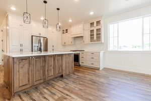Kitchen featuring appliances with stainless steel finishes, baseboards, light wood-type flooring, a kitchen island with sink, and decorative backsplash