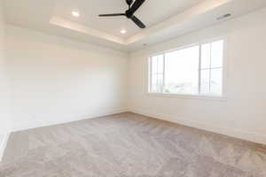 Carpeted spare room featuring baseboards, a raised ceiling, recessed lighting, and a ceiling fan