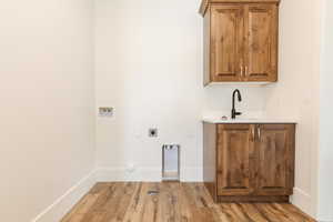 Laundry room with washer hookup, electric dryer hookup, cabinet space, light wood-style flooring, and baseboards