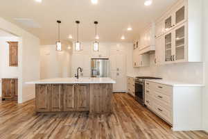Kitchen with stainless steel appliances, light wood-style flooring, light countertops, a center island with sink, and decorative backsplash
