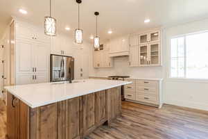 Kitchen featuring appliances with stainless steel finishes, baseboards, light wood-style floors, tasteful backsplash, and a center island with sink