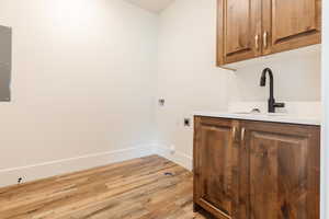 Washroom with electric dryer hookup, cabinet space, light wood-style flooring, baseboards, and hookup for a washing machine