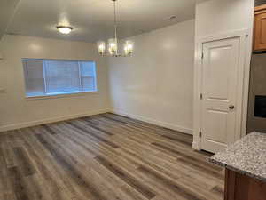 Unfurnished dining area featuring wood finished floors, a chandelier, a textured ceiling, and baseboards