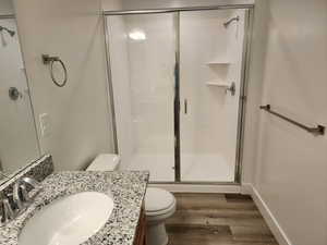 Full bathroom with toilet, a stall shower, wood finished floors, and vanity