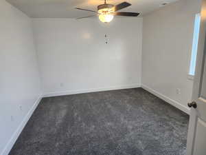 Spare room with a ceiling fan, dark colored carpet, and baseboards