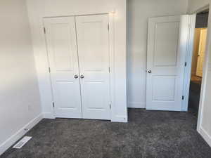 Unfurnished bedroom with dark carpet, baseboards, and a closet
