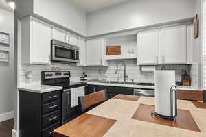 Kitchen with stainless steel appliances, white cabinets, light countertops, a sink, and dark cabinetry