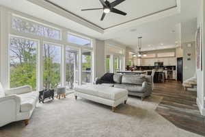 Living room featuring dark wood-type flooring, ceiling fan, ornamental molding, a tray ceiling, and recessed lighting
