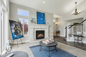 Living room featuring stairway, a chandelier, a glass covered fireplace, high vaulted ceiling, and baseboards