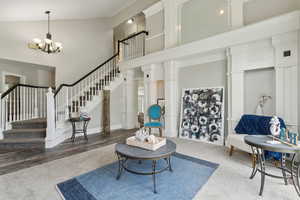 Living room featuring a towering ceiling, a chandelier, stairs, carpet flooring, and decorative columns