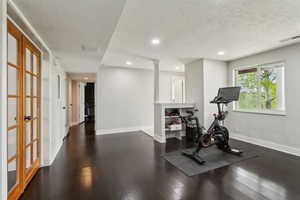 Exercise room featuring a textured ceiling, recessed lighting, baseboards, dark wood-style floors, and decorative columns