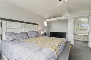 Carpeted bedroom featuring lofted ceiling, multiple windows, ensuite bathroom, and decorative columns