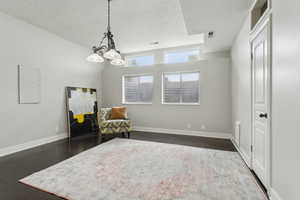 Living area with a textured ceiling, a chandelier, dark wood finished floors, and baseboards