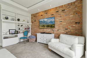 Living area featuring carpet, brick wall, built in shelves, and ornamental molding