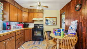 Kitchen featuring black range with electric stovetop, under cabinet range hood, light countertops, decorative backsplash, and a ceiling fan