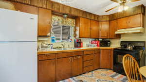 Kitchen with black appliances, under cabinet range hood, a sink, decorative backsplash, and a ceiling fan