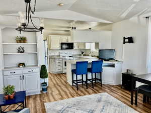 Kitchen featuring white appliances, a peninsula, a sink, open shelves, and lofted ceiling