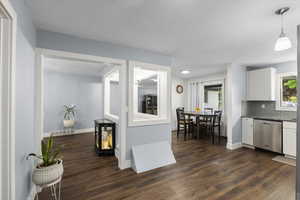 Kitchen with stainless steel dishwasher, white cabinets, dark wood-type flooring, backsplash, and baseboards