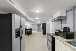 Kitchen with fridge with ice dispenser, range with two ovens, black microwave, under cabinet range hood, and a textured ceiling