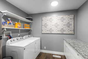 Main floor Clothes washing area with washing machine and dryer, dark wood finished floors, baseboards, and cabinet space