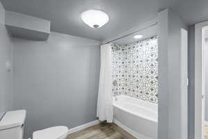 Bathroom featuring toilet, wood finished floors, shower / tub combo with curtain, and baseboards