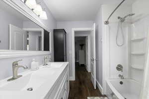 Full bathroom with shower / washtub combination, wood finished floors, double vanity, and baseboards