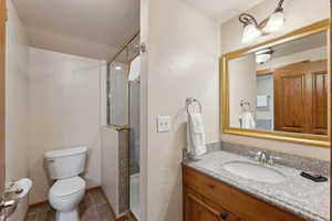 Bathroom featuring toilet, a stall shower, tile patterned floors, vanity, and baseboards
