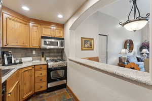 Kitchen featuring gas range, stainless steel microwave, stone tile floors, tasteful backsplash, and light countertops