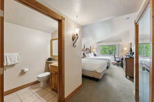 Bedroom featuring baseboards, lofted ceiling, a textured ceiling, and light tile patterned flooring
