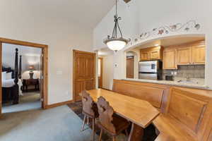 Dining area featuring high vaulted ceiling, light colored carpet, and baseboards