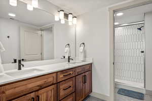 Bathroom with a tile shower, double vanity, baseboards, and recessed lighting