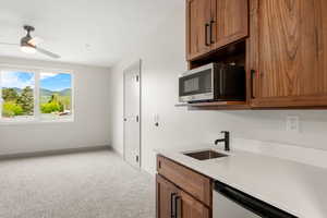 Kitchen featuring stainless steel microwave, a sink, light colored carpet, and brown cabinets