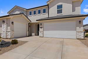 View of front of property with stone siding, driveway, an attached garage, and stucco siding