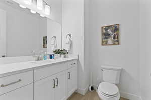 Bathroom featuring baseboards, toilet, wood finished floors, and vanity