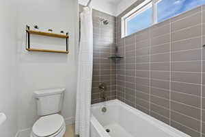 Full bathroom with toilet, baseboards, and shower / bath combo with shower curtain