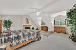 Carpeted bedroom featuring vaulted ceiling, baseboards, a fireplace, and a ceiling fan
