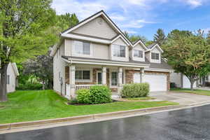 View of front of property with a porch, concrete driveway, a front lawn, stone siding, and an attached garage