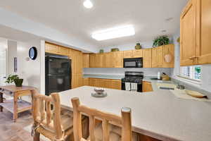Kitchen featuring black appliances, a sink, a peninsula, light countertops, and light brown cabinets