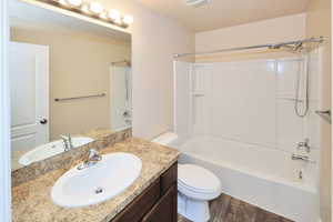 Bathroom featuring wood finished floors, bathing tub / shower combination, toilet, and vanity