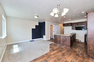Kitchen with a chandelier, a kitchen island, dark brown cabinets, a textured ceiling, and baseboards