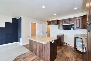 Kitchen featuring stainless steel microwave, dark brown cabinetry, dark wood finished floors, light countertops, and a textured ceiling