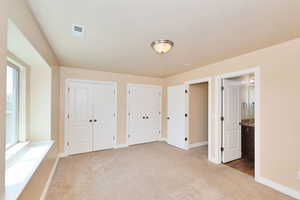 Unfurnished bedroom with carpet flooring, two closets, baseboards, and connected bathroom