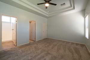 Unfurnished bedroom featuring carpet floors, baseboards, a raised ceiling, and ensuite bathroom