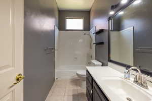 Bathroom with toilet, vanity, tile patterned flooring, shower / washtub combination, and baseboards
