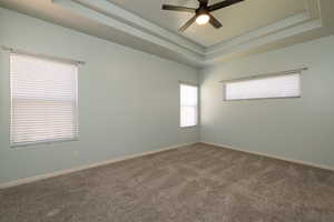 Bedroom with ensuite bathroom, walk in closet , raised ceiling, and ceiling fan.