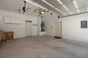 Garage with strapped water heater, electric panel, door to back patio, and a garage door opener