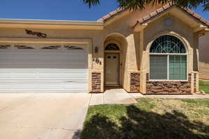 Property entrance featuring driveway, stucco siding, an attached garage, and stone siding