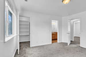Primary bedroom with carpet flooring, baseboards, a walk in closet, ensuite bathroom, and a closet