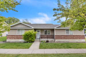 Ranch-style home with brick siding, a porch, a front yard, and roof with shingles