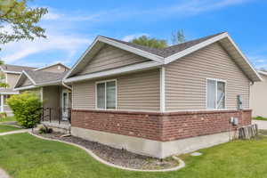 View of property exterior with brick siding, a yard, and roof with shingles